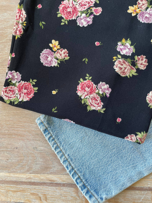 Pink print ECOVERO viscose Moroccan crepe by Atelier 27, pink and mauve rose bouquets scattered on a black ground, folded over denim