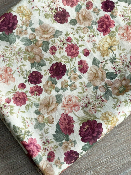 Alessia print cotton satin by Atelier 27, dense plum, burgundy and dusty rose blooms with sage foliage on ivory, folded on grey wood