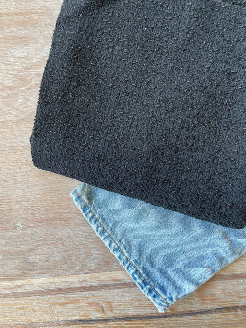 Twist jacquard fabric by Atelier 27, dense black bouclé-textured weave, folded over denim on a pale wood surface