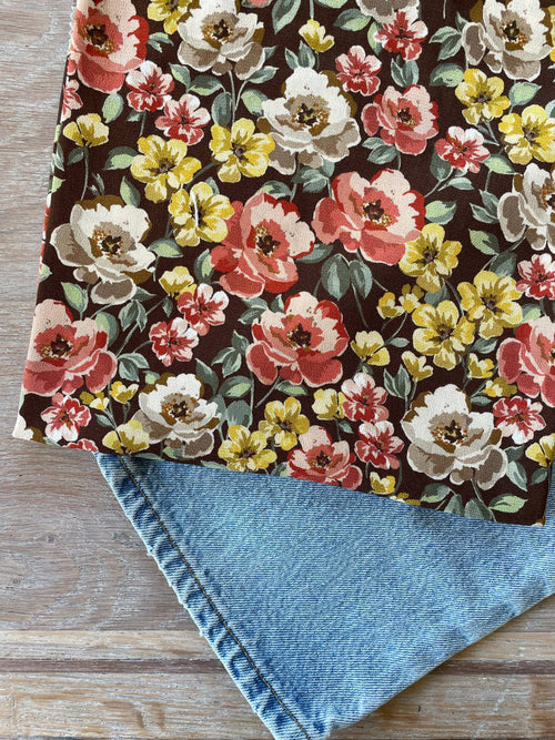 Inaya print ECOVERO viscose Moroccan crepe by Atelier 27, dense poppy-coral, cream and yellow blooms with sage leaves on a chocolate-brown ground, folded over denim