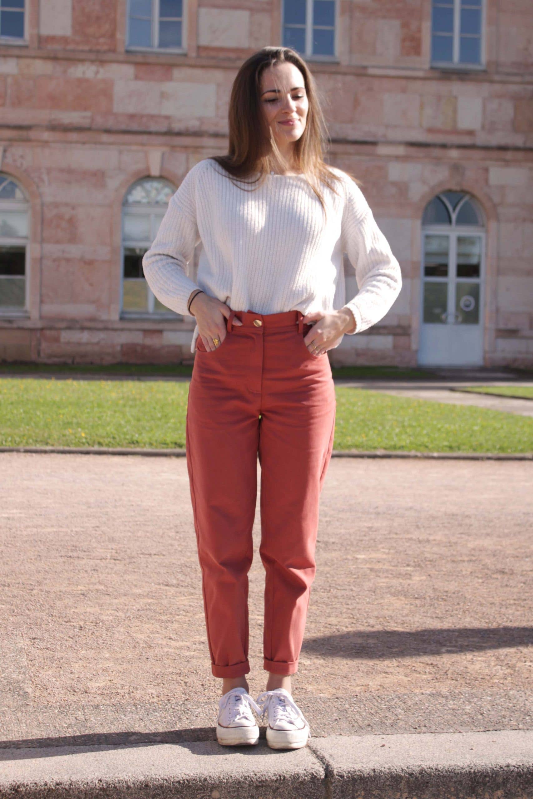 Jade Trousers sewing pattern by Cha' coud sewn in rust-red fabric, worn with a white sweater, front view