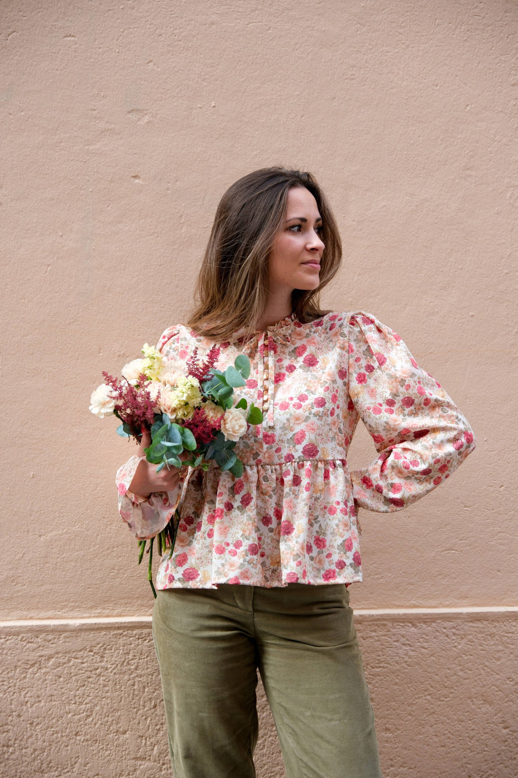 Alessia Blouse sewing pattern by Cha' coud sewn in rose floral fabric, worn with olive corduroy trousers, holding a bouquet