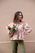 Alessia Blouse sewing pattern by Cha' coud sewn in rose floral fabric, worn with olive corduroy trousers, holding a bouquet