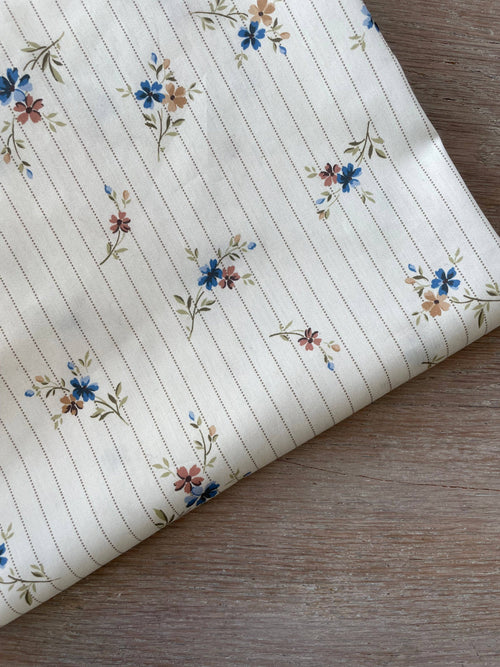Hector print cotton satin by Atelier 27, blue and dusty-rose floral sprigs over fine olive pinstripes on ivory, folded corner on pale wood
