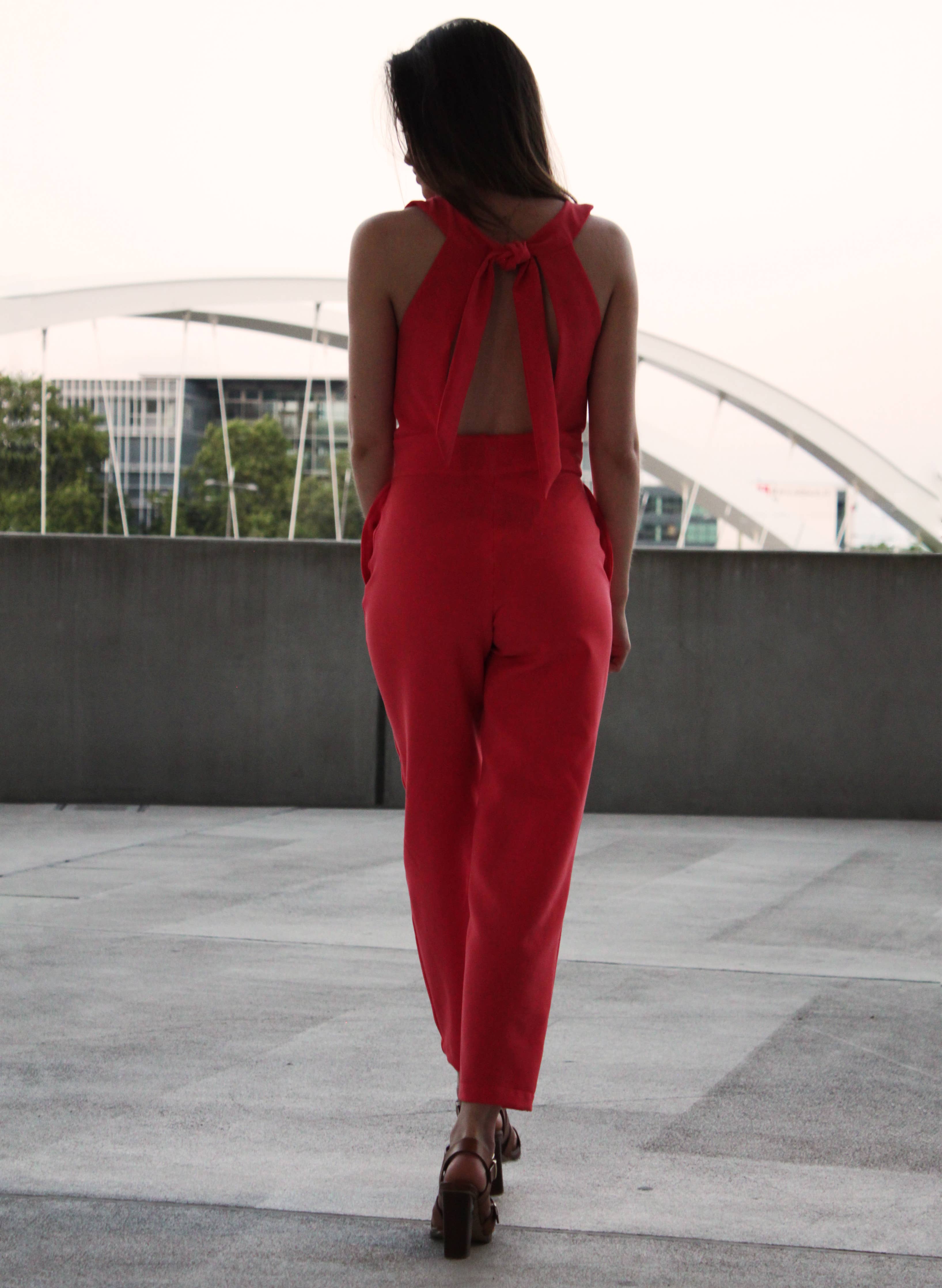 Back view of the red Aurore Jumpsuit by a bridge