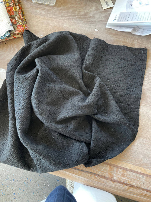 Twist black jacquard gathered in deep folds on a worktable, showing its weight and soft drape with faint metallic glints | Atelier 27