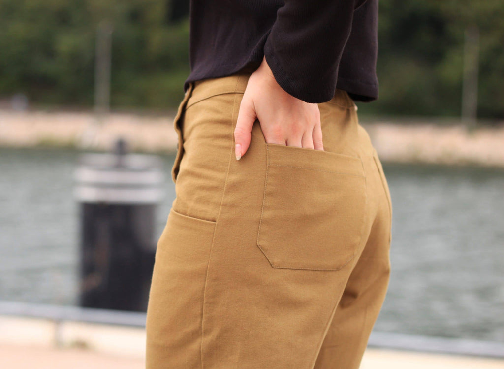 Close-up of the Thaïs Trousers back patch pocket in camel twill by the water