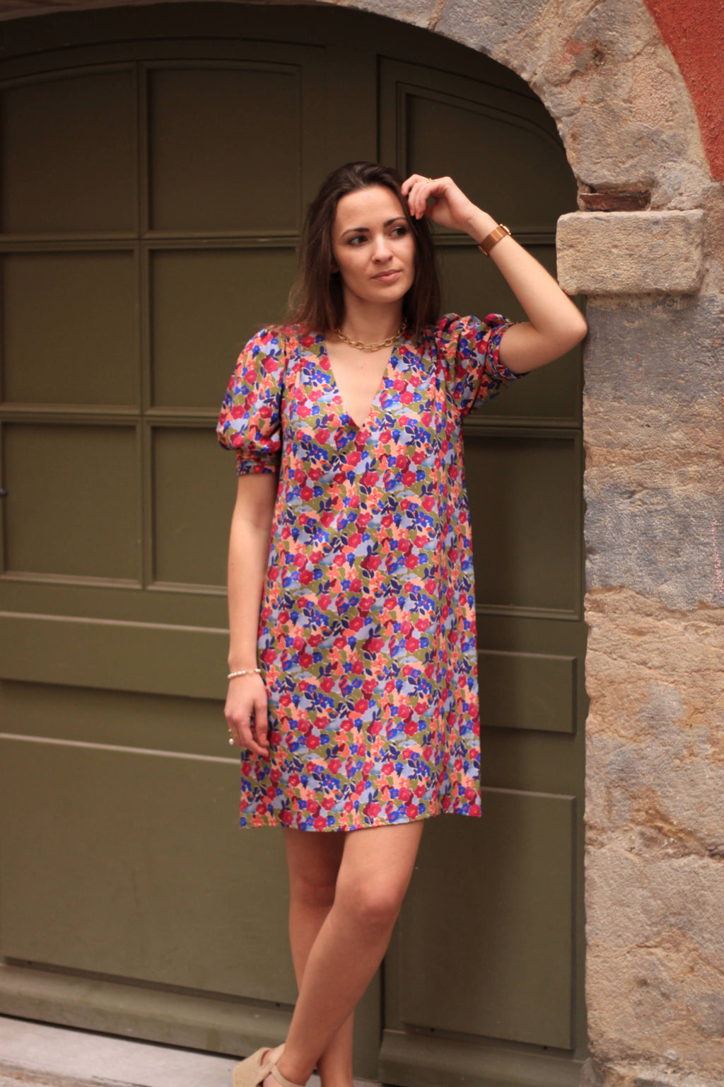 Calie Dress sewing pattern by Cha' coud sewn in bright floral viscose with puff sleeves, front view by a green door