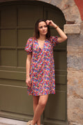 Calie Dress sewing pattern by Cha' coud sewn in bright floral viscose with puff sleeves, front view by a green door